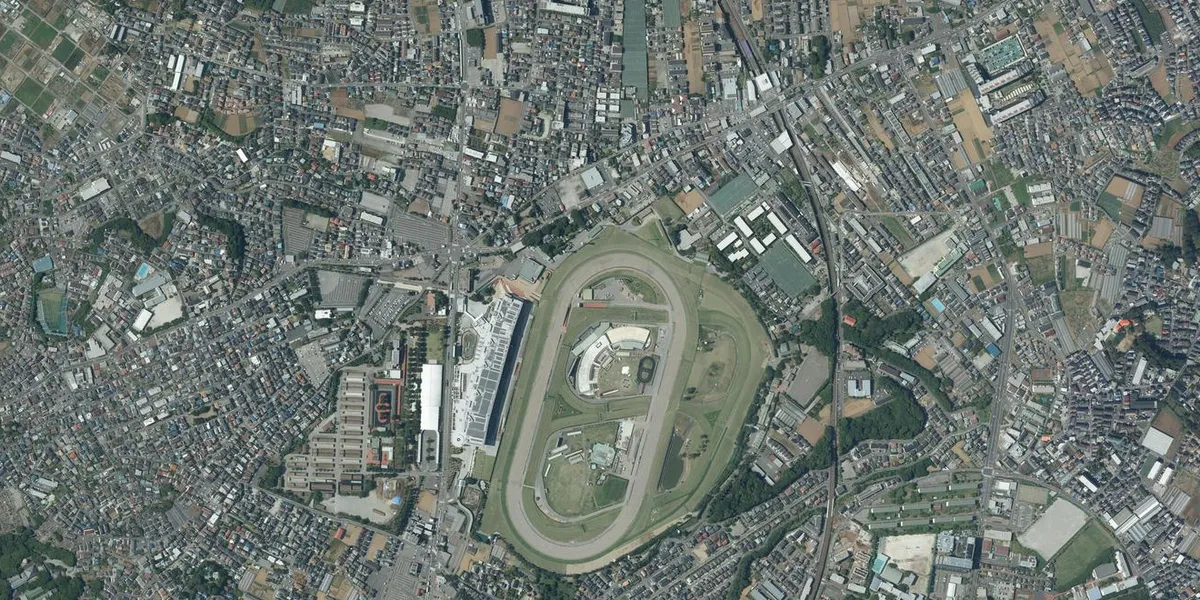 中山競馬場を真上から写した航空写真。楕円のコースの西側にスタンドがあり、東側を線路が通っています